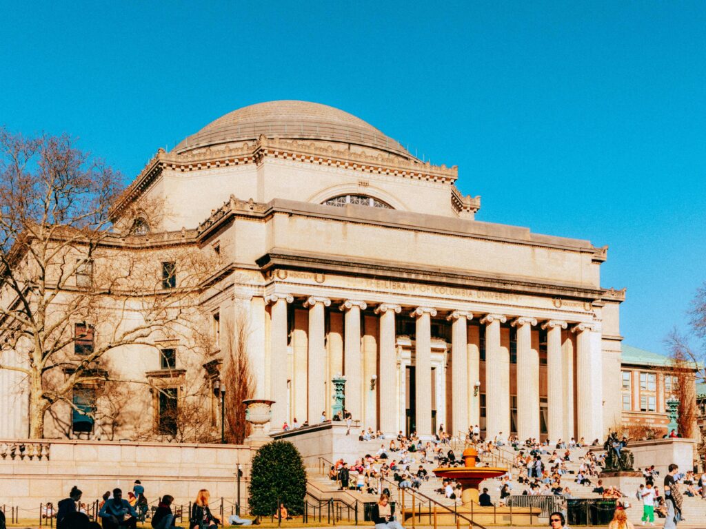 Historic library at Columbia University with people gathered on steps under clear sky.
